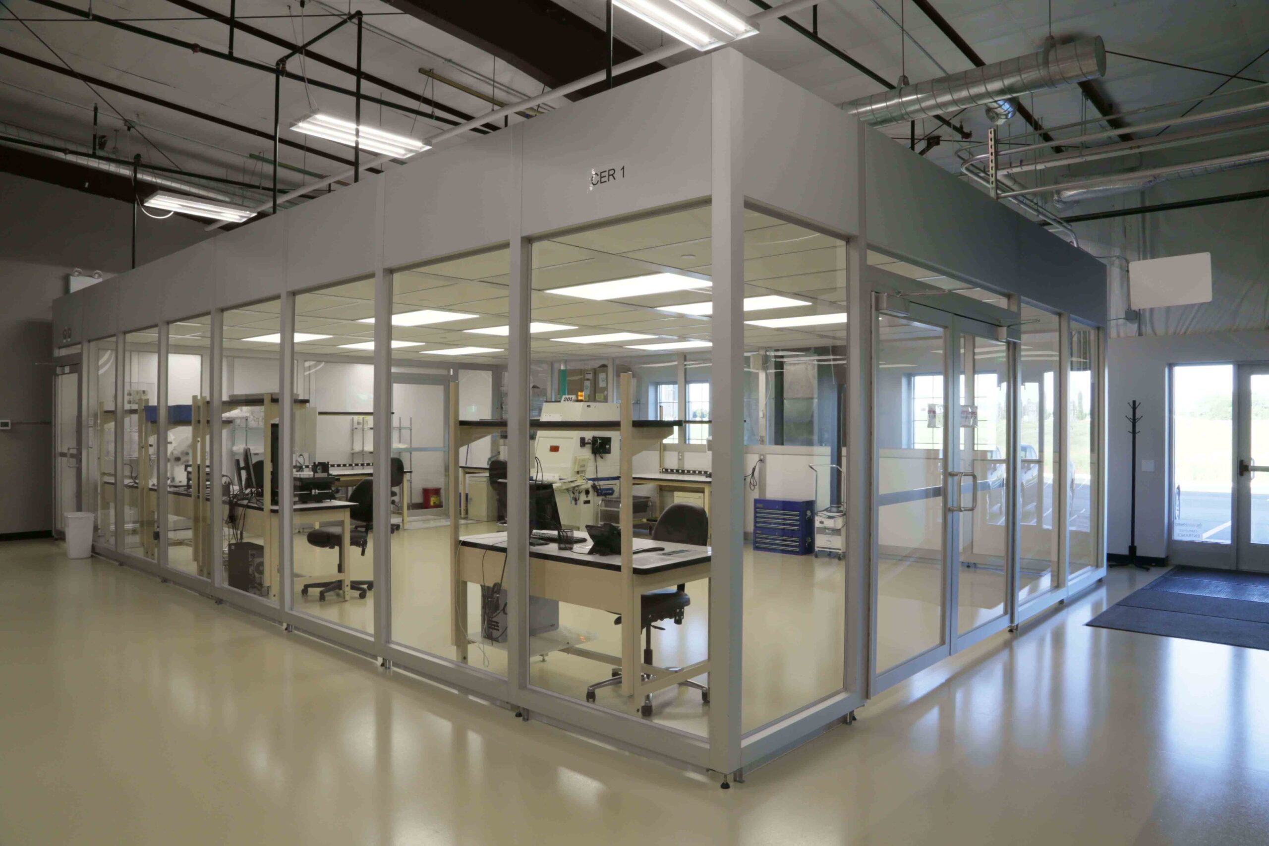 Outside cleanroom with lasers and computers on computer desks inside the cleanroom